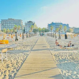 SM Hotels: ti meriti il mare tutto l’anno Spiaggia con ombrelloni chiusi e palme davanti a edifici