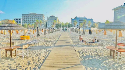 SM Hotels: ti meriti il mare tutto l’anno Spiaggia con ombrelloni chiusi e palme davanti a edifici