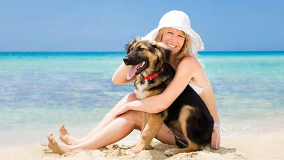 SM Hotels: ti meriti il mare tutto l’anno Donna sorridente con cappello bianco abbraccia cane sulla spiaggia