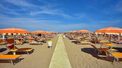 SM Hotels: ti meriti il mare tutto l’anno Ombrelloni arancioni e sdraio su una spiaggia sabbiosa sotto un cielo blu