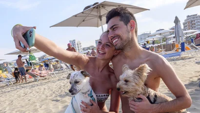 SM Hotels: ti meriti il mare tutto l’anno Coppia scatta selfie sulla spiaggia con due cani sotto ombrelloni