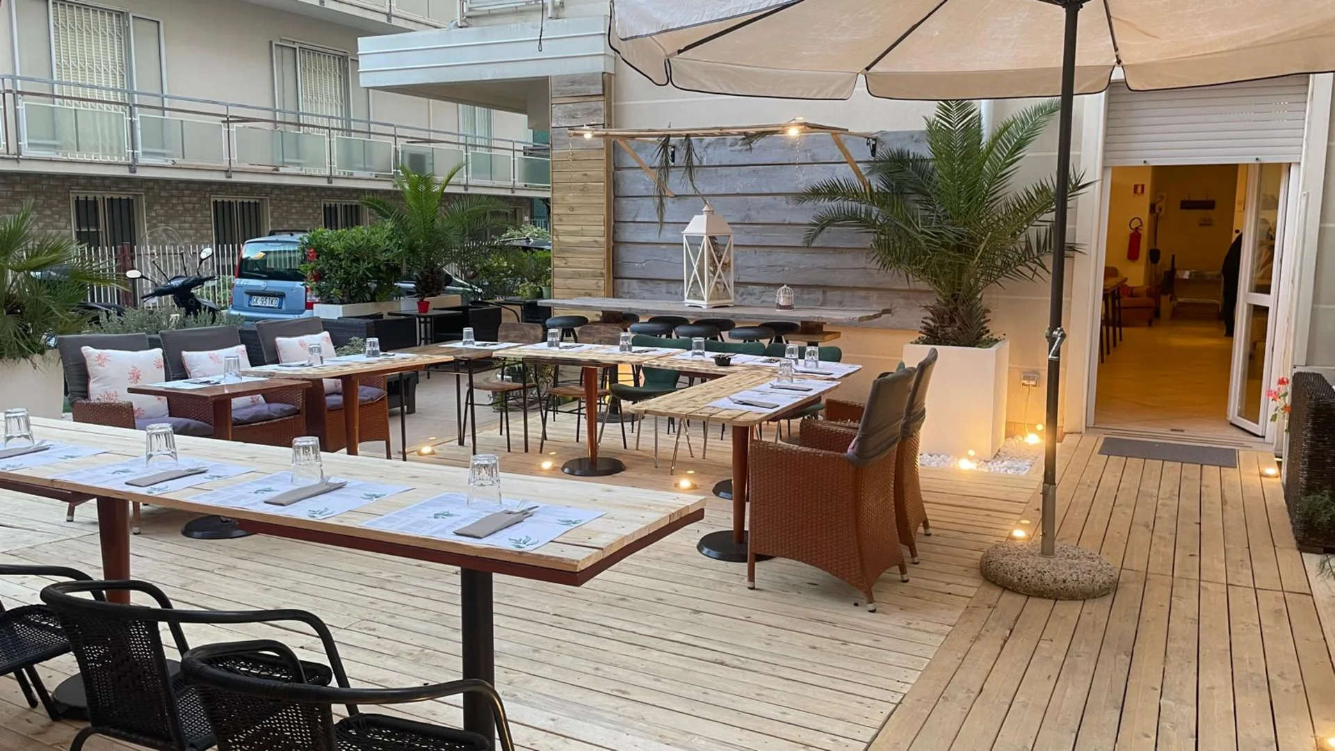SM Hotels: ti meriti il mare tutto l’anno Tavoli e sedie all'aperto in un ristorante con ombrellone e luci a sospensione