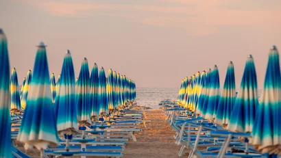 SM Hotels: ti meriti il mare tutto l’anno Ombrelloni azzurri chiusi in fila su una spiaggia al tramonto