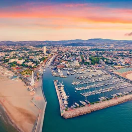 SM Hotels: ti meriti il mare tutto l’anno Veduta aerea del porto e della spiaggia al tramonto con la città e le montagne sullo sfondo